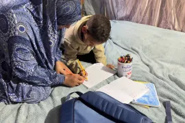 Nibal Abu Armana teaching her son Muhammed in their displacement tent in Nusairat Camp [Ola Al-Asi/ Al Jazeera]