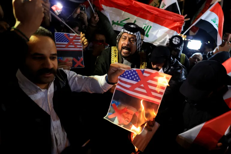 A supporter of Iraqi Shi'ite armed groups burns a poster with red X marks on the images of a U.S. flag and U.S. President Donald Trump during a protest against what they say is U.S. interference in Iraq’s sovereignty near the entrance of the Green Zone, home to the U.S. embassy and other missions, in Baghdad,Iraq, January 28, 2026. REUTERS/Thaier Al-Sudani